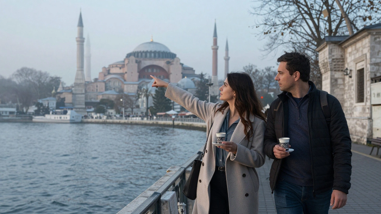 A woman pointing toward Hagia Sophia at dawn while sharing coffee with a man along the Bosphorus shore.